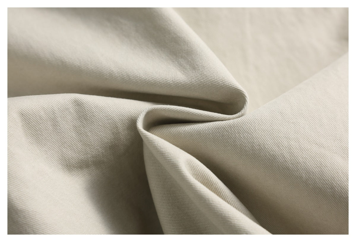Close-up of light beige fabric draped to show its fine diagonal weave.
