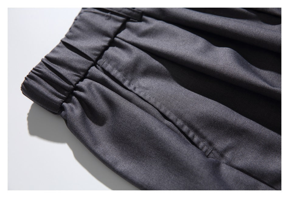 Close-up of dark charcoal trousers showing a gathered waistband and stitched seam.
