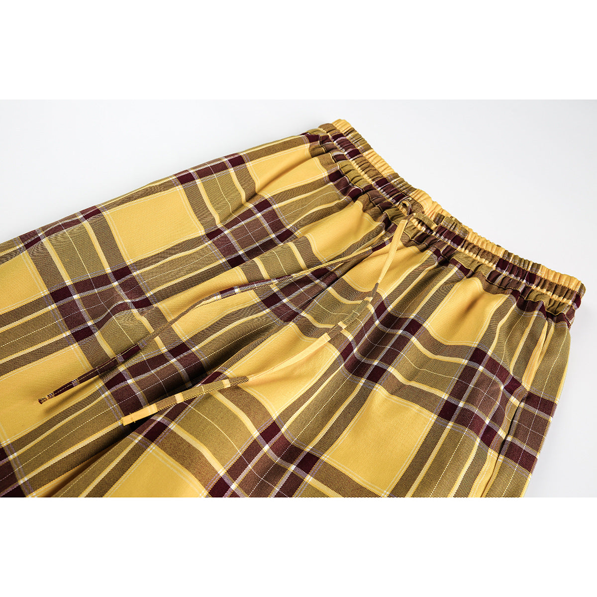 Close-up of mustard yellow plaid pants showing the gathered elastic waistband and matching drawstrings.