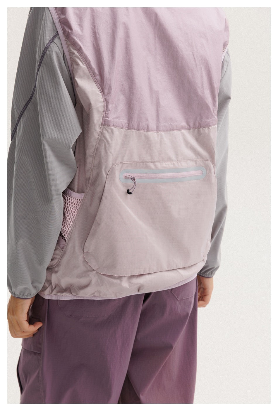 Close-up of the jacket's pale mauve back, showing a large zip pocket, mesh side panel, and gray sleeves.