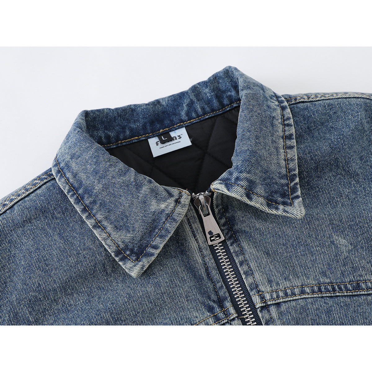 Close-up of a blue denim jacket collar, black lining, neck label, and front zipper.