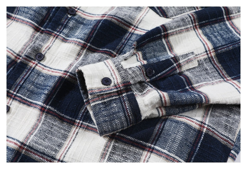 Close-up of the buttoned cuff and sleeve of a navy, white, gray, and red plaid shirt.