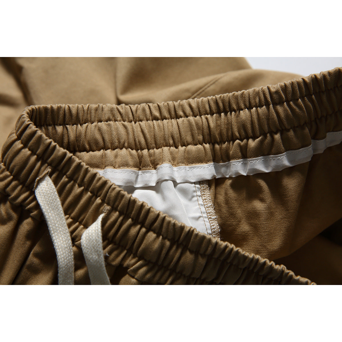 Inside close-up of tan trousers showing the elastic waistband, white lining and drawstrings.