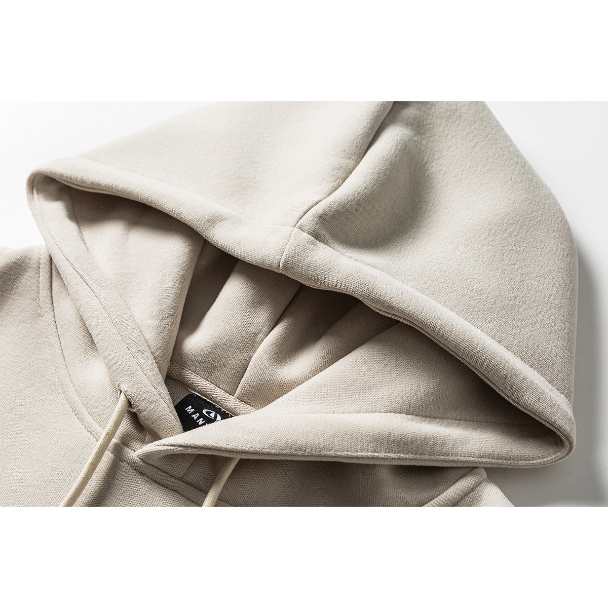 Close-up of a light beige hoodie showing its hood, seams, drawstring, and inner neck label.