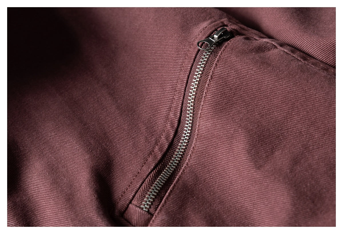 Close-up of a dark metal zipper and stitching on burgundy fabric.