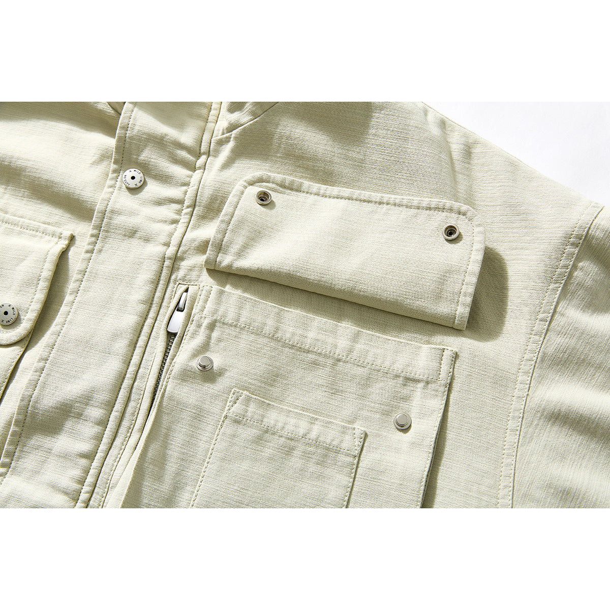 Close-up of a pale beige jacket showing snap-flap chest pockets and a vertical zipper pocket.