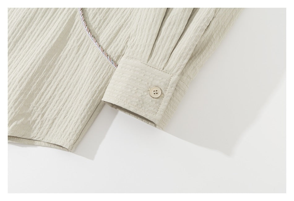 Close-up of a cream shirt sleeve and buttoned cuff with textured fabric and striped piping.