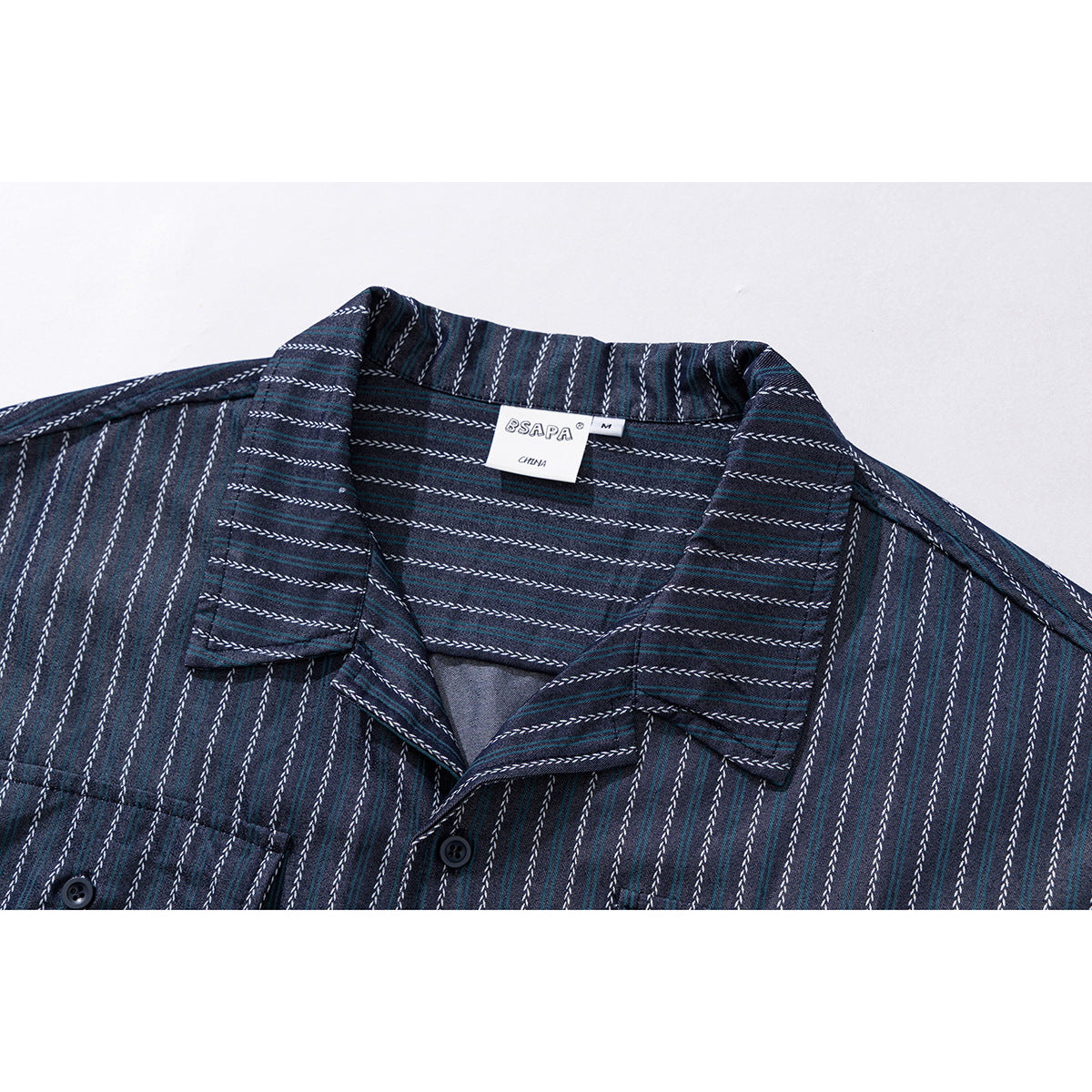 Close-up of a dark navy short-sleeve shirt collar with teal and white pinstripes, buttons, and a sewn-in label.