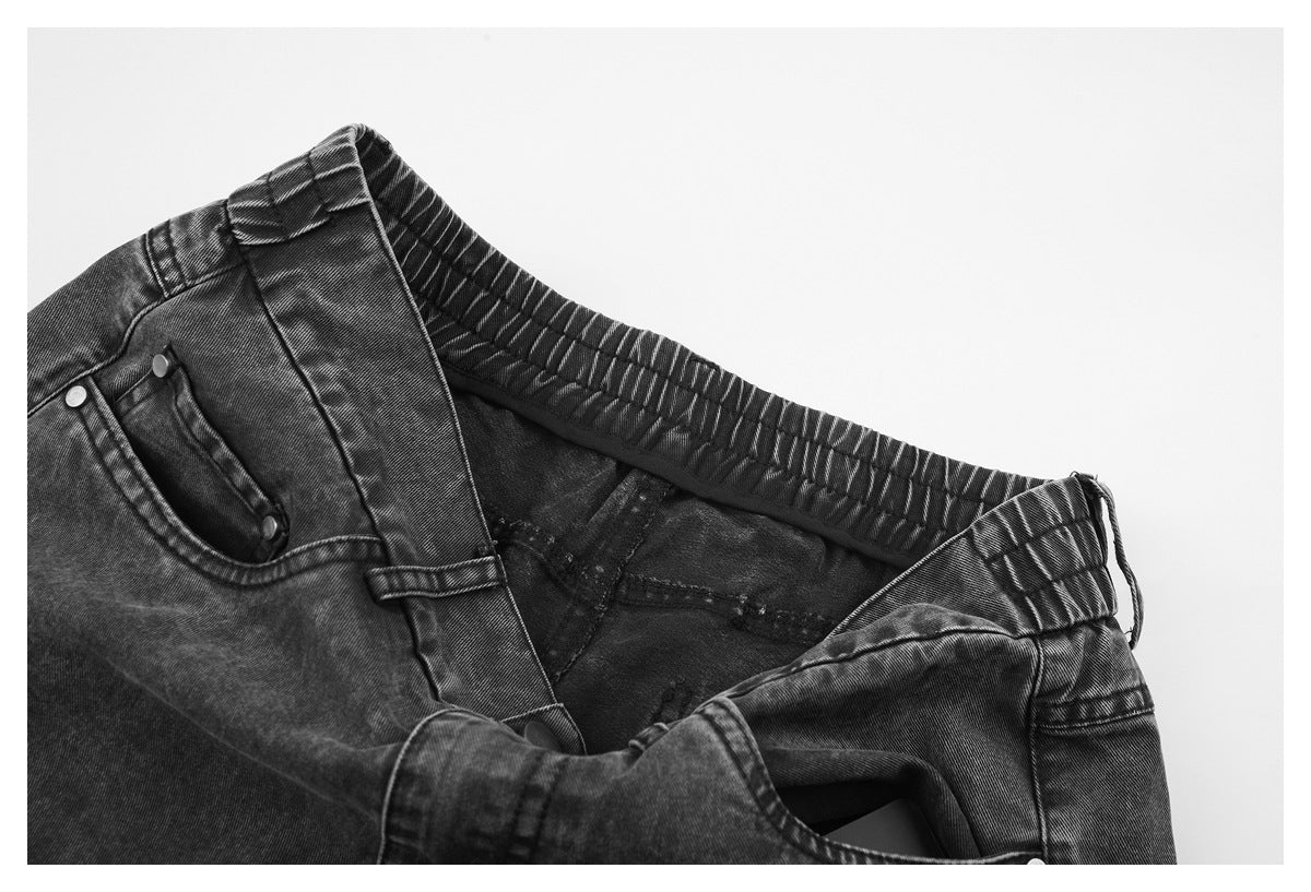 Close-up of charcoal gray jeans showing the elastic waistband, button fly, and front pocket.