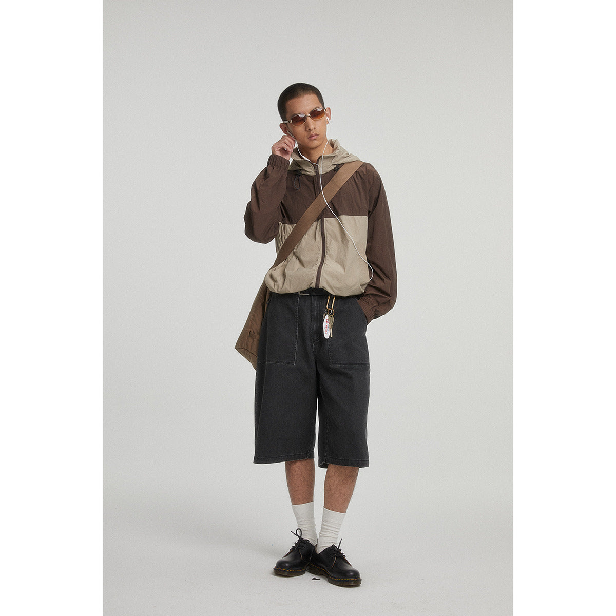 Model wearing a brown-and-beige color-block hooded jacket and black knee-length shorts.