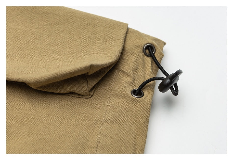 Close-up of tan trouser fabric with a black elastic drawcord and toggle at the edge.