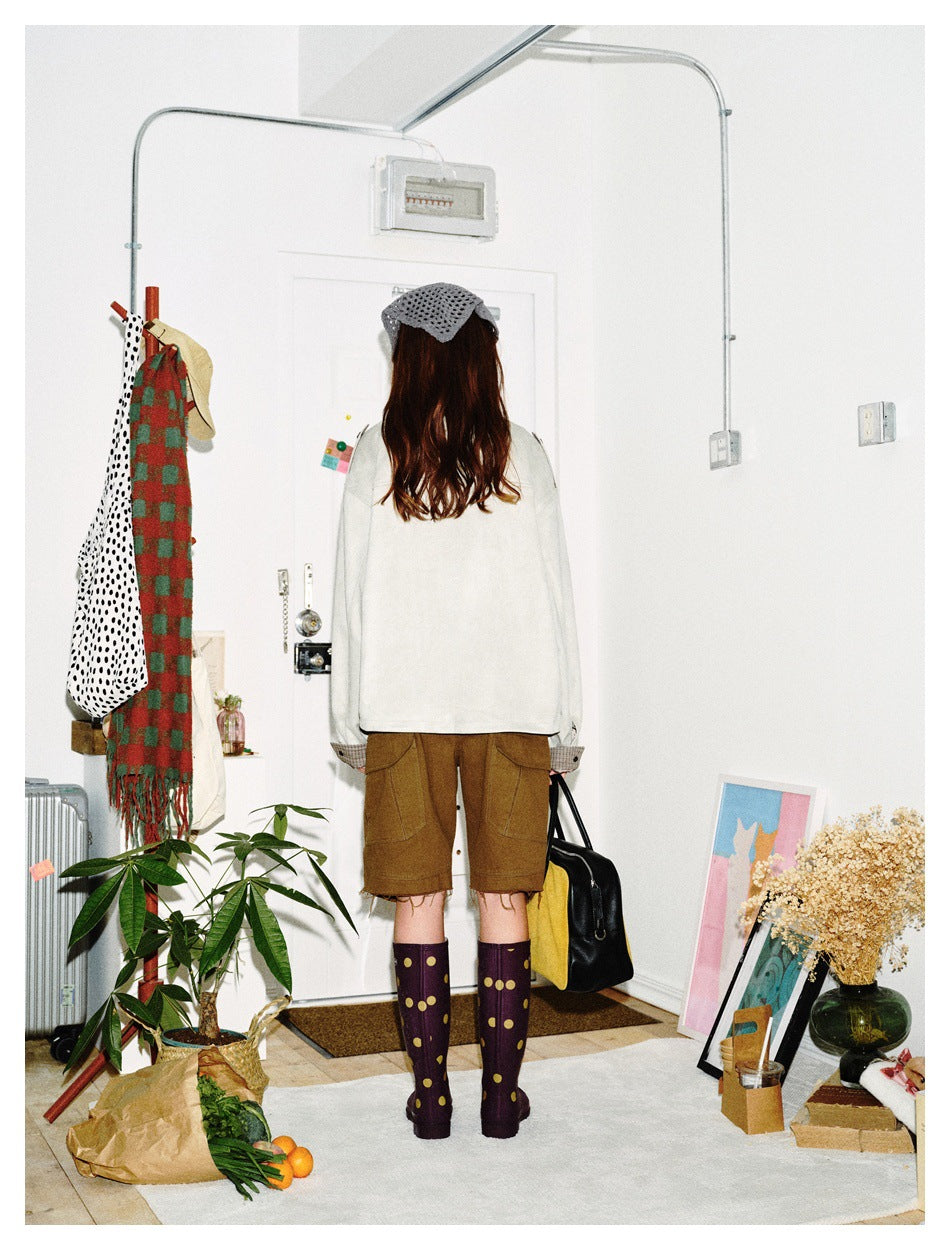 Rear view of a model in an ivory jacket with plaid cuffs, brown cargo shorts, and dark polka-dot boots.