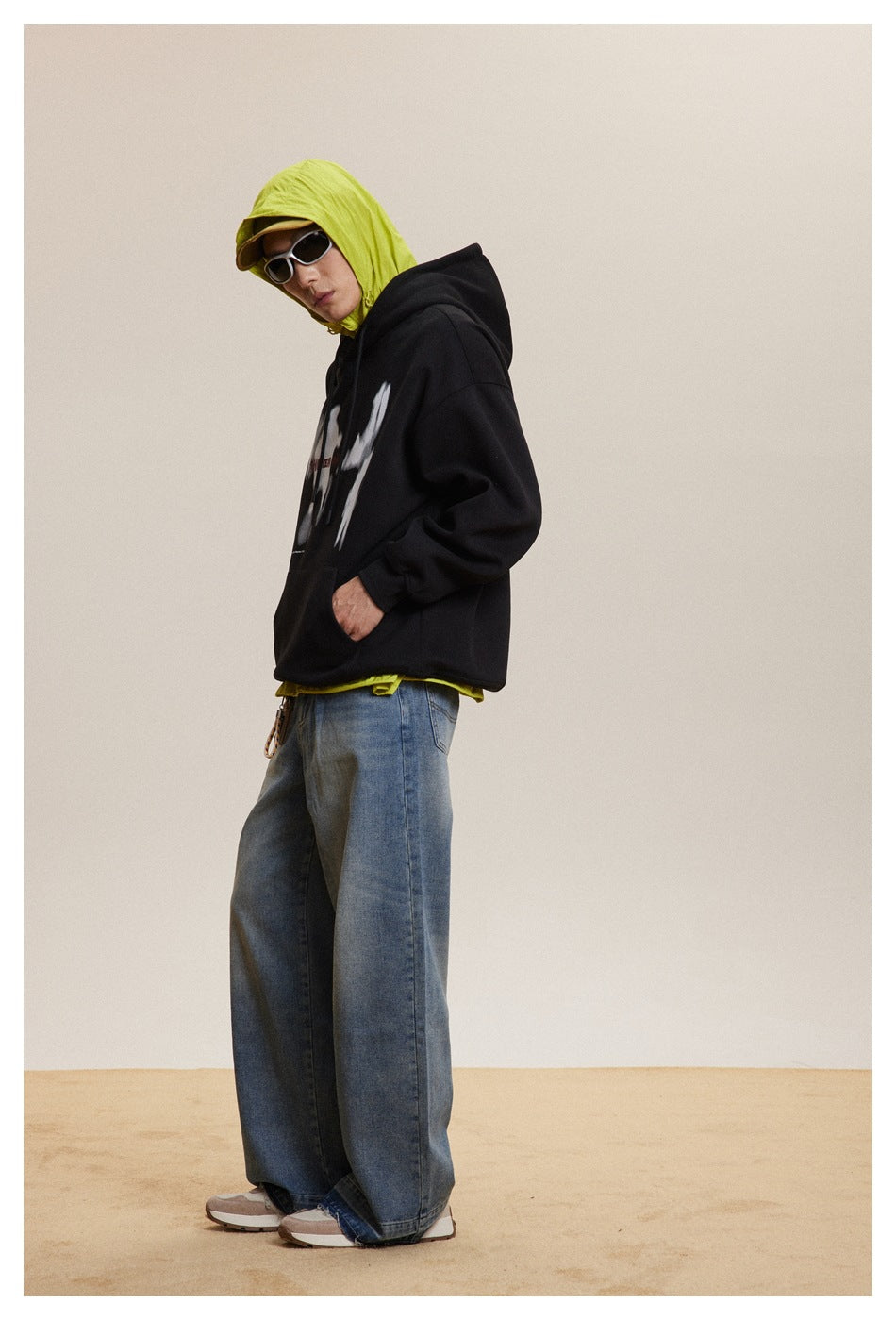 Side view of a person wearing a black graphic hoodie, neon yellow hooded layer, and wide blue jeans.