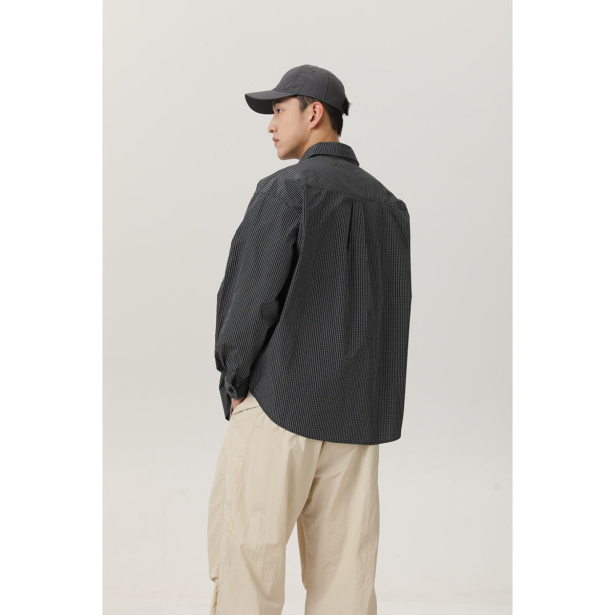 Rear three-quarter view of a model wearing a charcoal micro-check shirt with a back yoke and pleat.