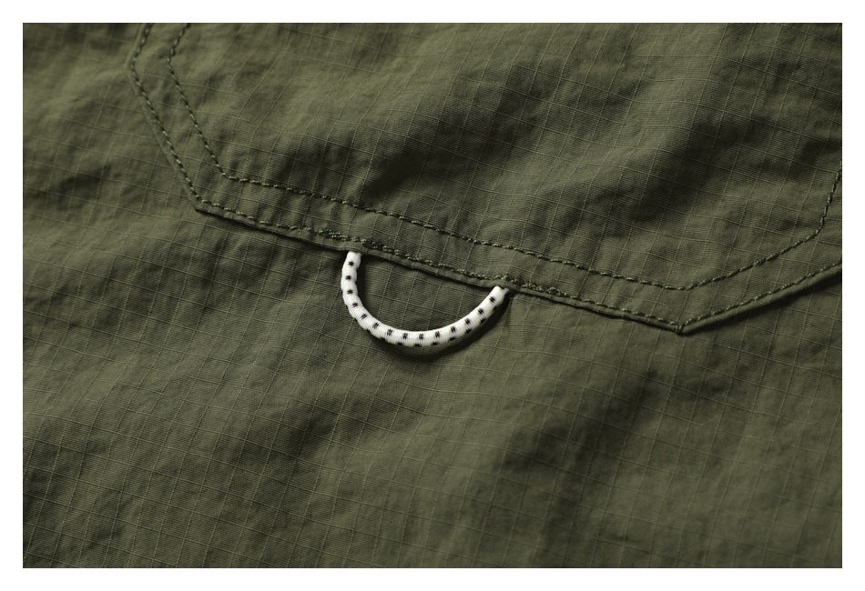 Close-up of a small white dotted loop attached beneath the dark olive shirt's pocket flap.