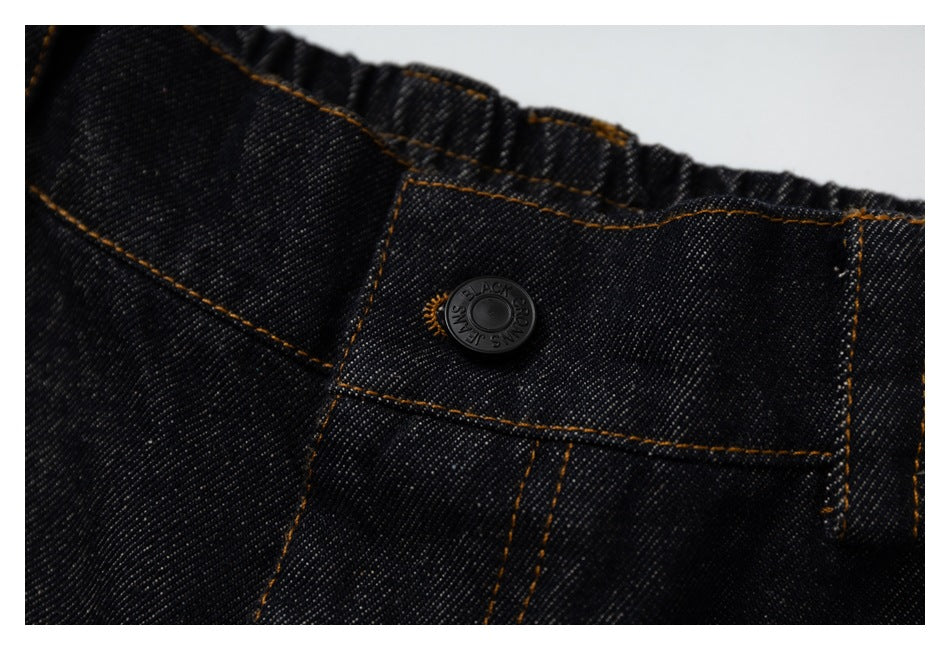 Close-up of dark denim jeans showing the black waistband button and orange-brown contrast stitching.