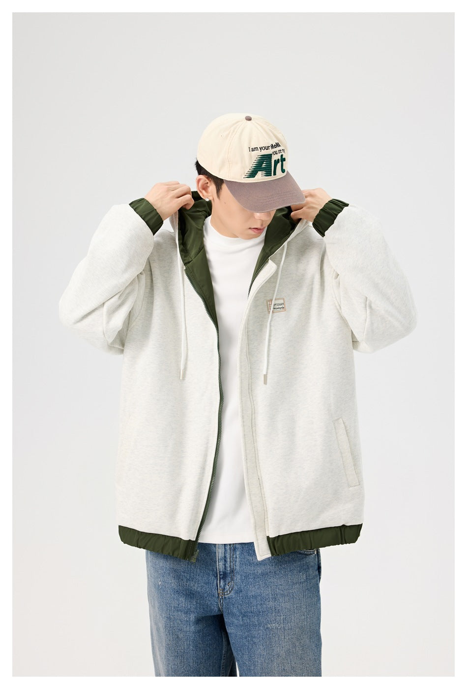 Model adjusting the hood of a light gray zip jacket with dark green lining and trim.