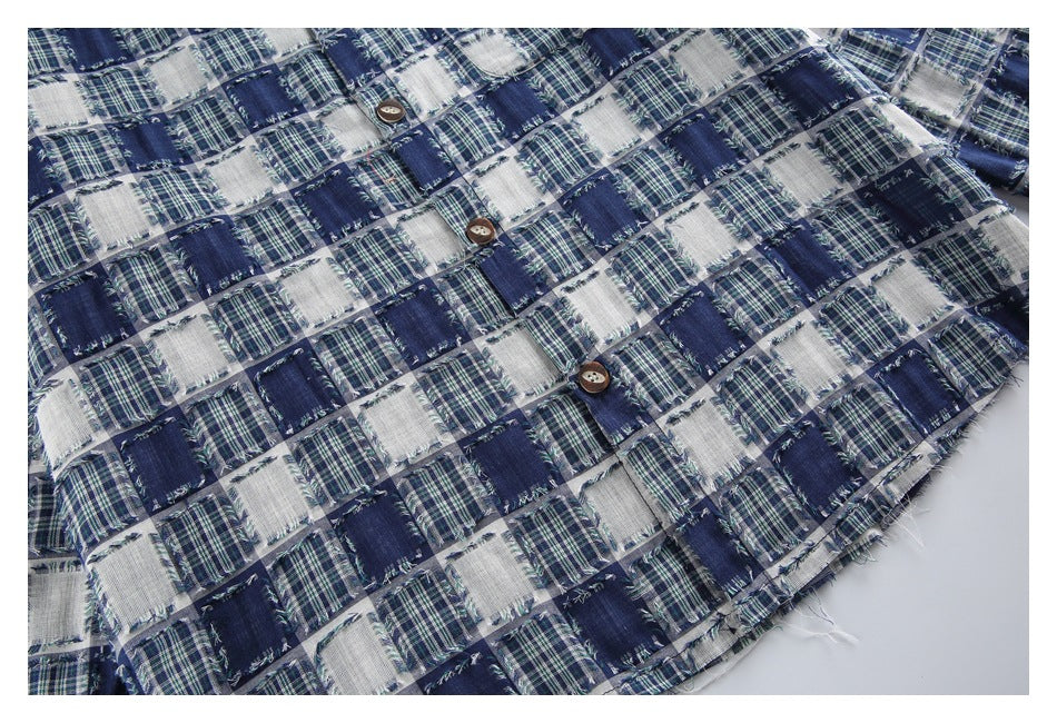 Flat-lay view of a blue, green and white patchwork plaid shirt front with buttons and frayed edges.