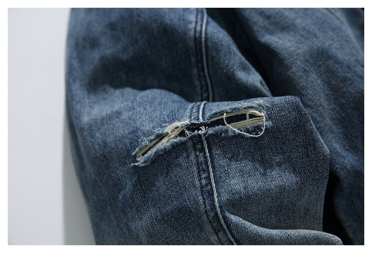 Close-up of a frayed tear with loose threads along a seam in blue denim.