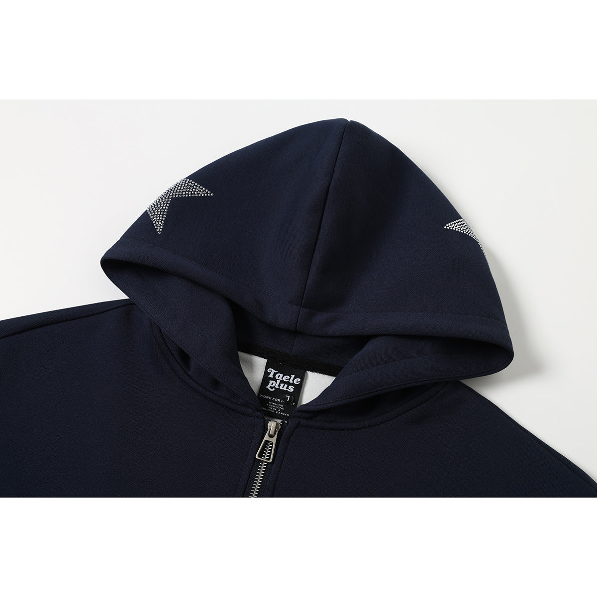 Close-up of a navy zip hoodie’s pointed hood, silver star accents, zipper, and English neck label.