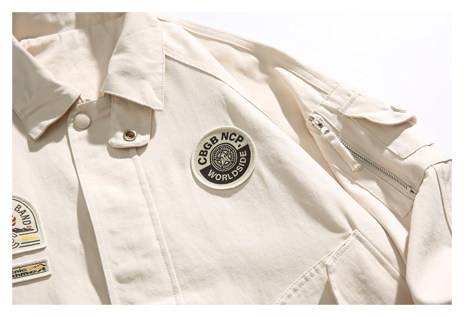 Close-up of an ivory jacket showing a round chest patch, part of two other patches, and a zippered sleeve pocket.