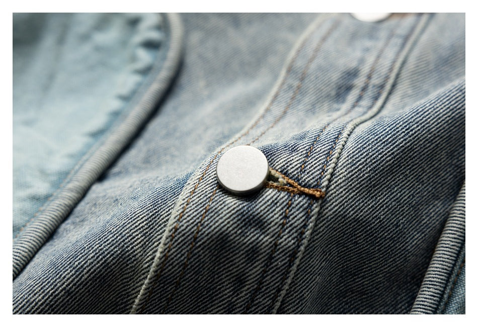 Close-up of a silver button and tan-stitched seams on faded blue denim.