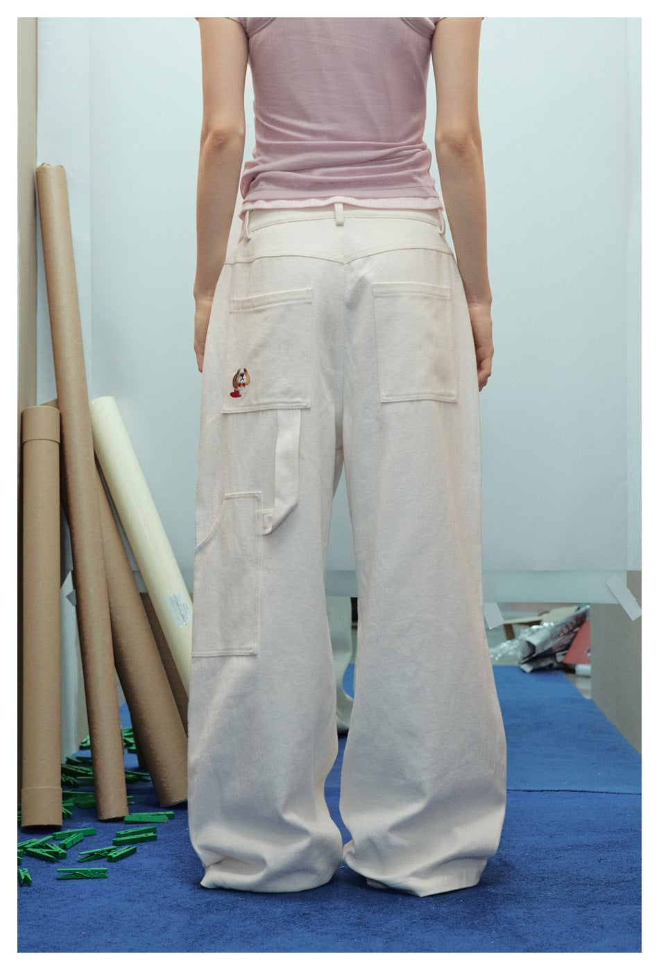 Back view of a model wearing cream wide-leg trousers with two rear patch pockets and a side cargo pocket.