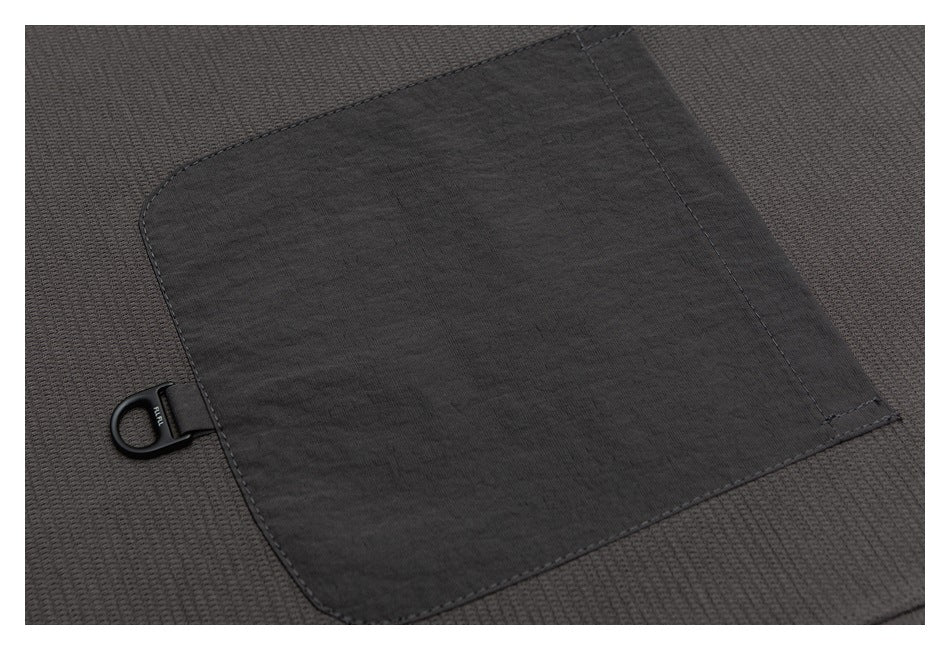 Close-up of a dark charcoal garment pocket with a black loop attachment.