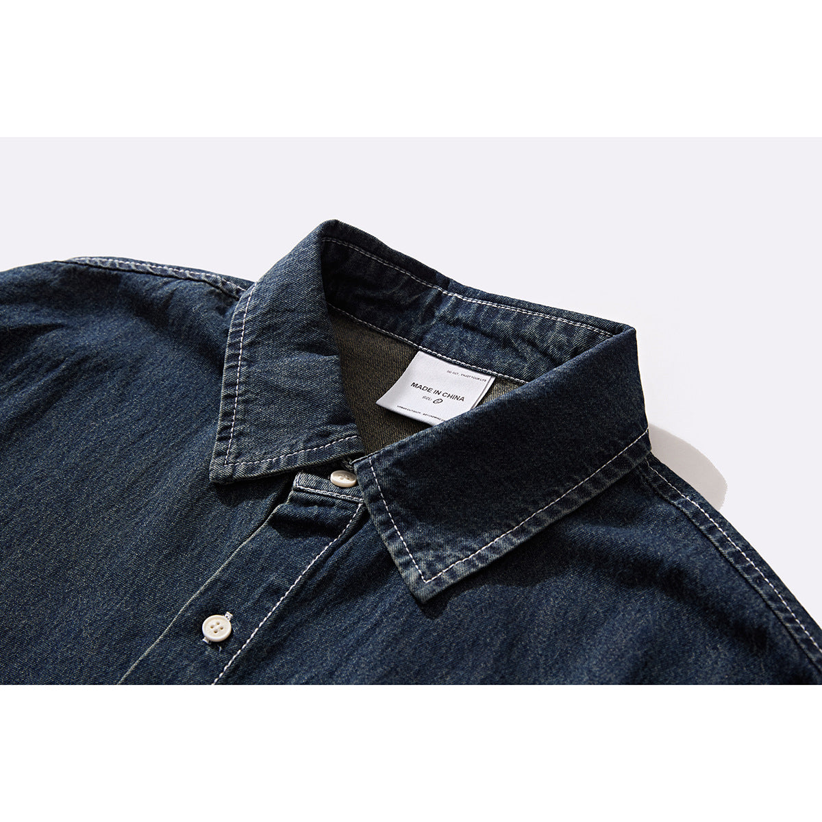 Close-up of a dark indigo denim shirt collar and button placket with light contrast stitching and a white neck label.