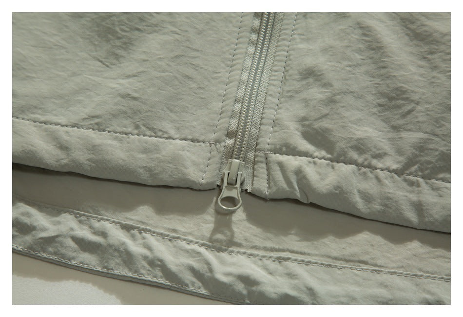 Close-up of a pale sage garment hem with a light-colored zipper, stitched seams, and crinkled fabric.