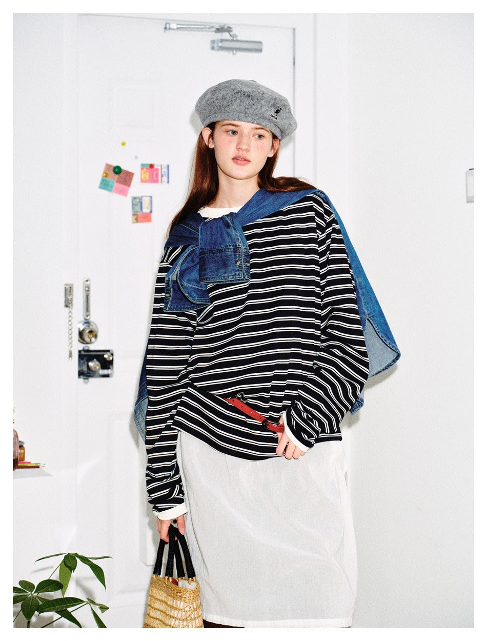 Model wearing an oversized black-and-white striped top with a white apron-style layer, red belt and blue denim draped over