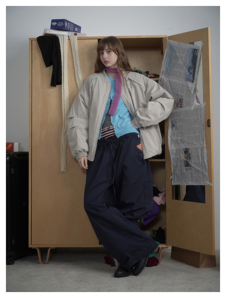 Model wearing an open light beige-gray oversized jacket over a blue cardigan, with loose navy trousers.