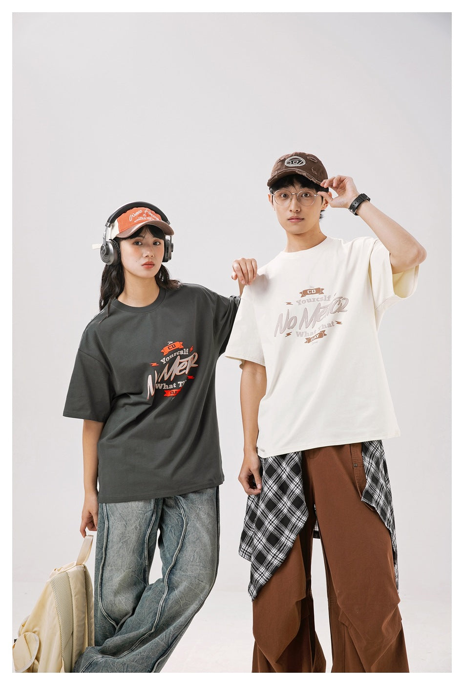 Two models pose in charcoal and off-white oversized graphic T-shirts, showing the fronts.