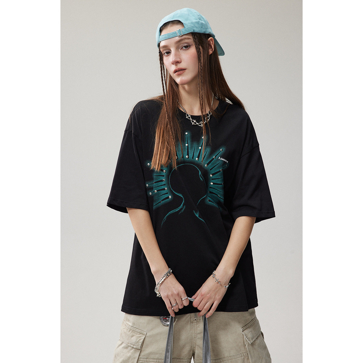 Model wearing an oversized black T-shirt with a teal radiating silhouette graphic and metallic studs.
