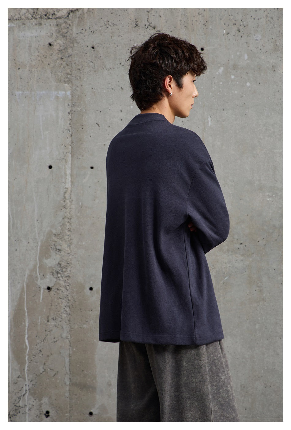 Side and rear view of a model wearing an oversized navy crewneck with a plain back and wide gray trousers.