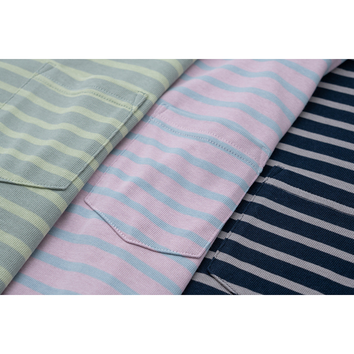 Three folded striped T-shirts in sage green, pink, and navy, with chest pockets visible.