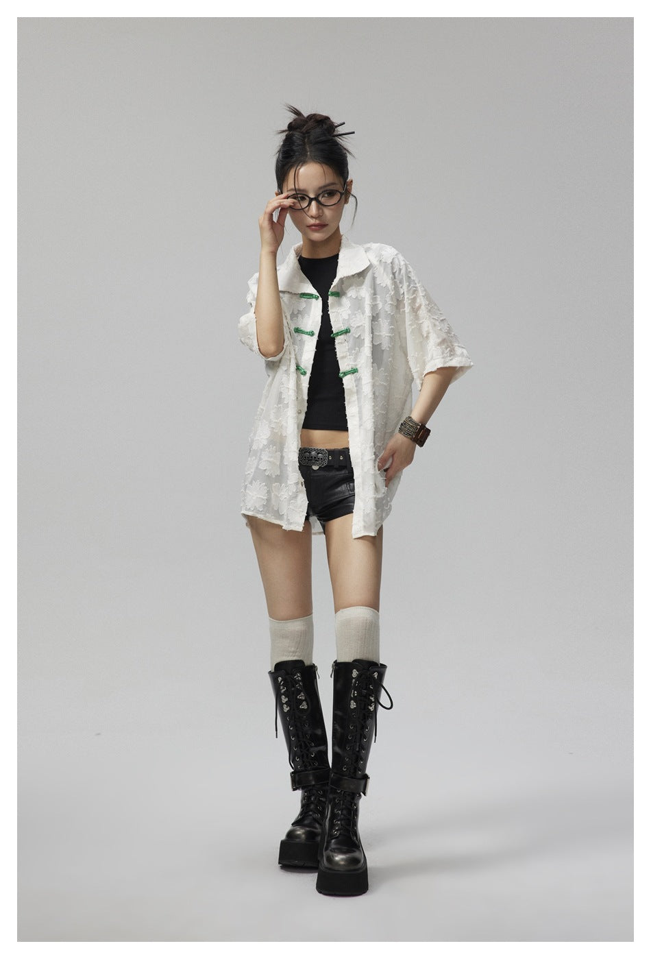 Full-length model wearing a white floral shirt with green frog closures over a black top and shorts.