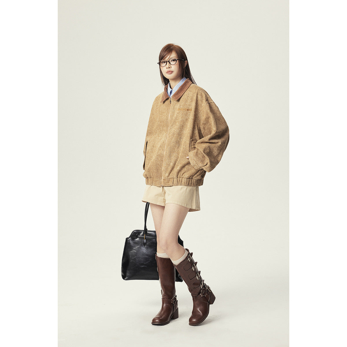 Model wearing an oversized tan zip jacket with a brown collar, beige shorts, and tall brown boots.