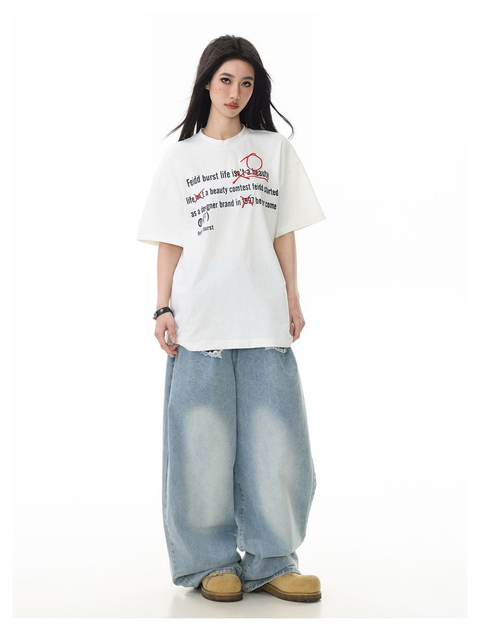 Model wearing oversized white graphic T-shirt with light-wash wide-leg jeans and tan shoes, full-length front view