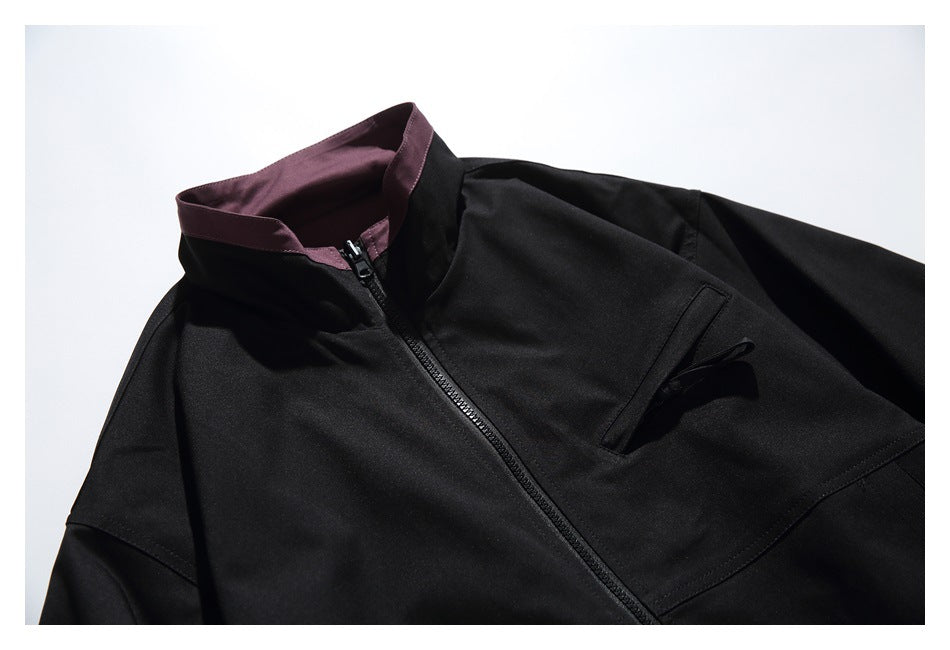 Flat-lay upper front of a black zip jacket with a burgundy stand collar and a vertical chest pocket.