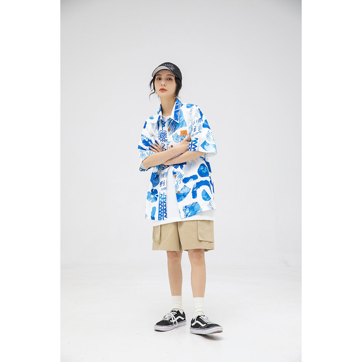 Model wearing a blue-and-white printed short-sleeve shirt with beige shorts and a black cap.