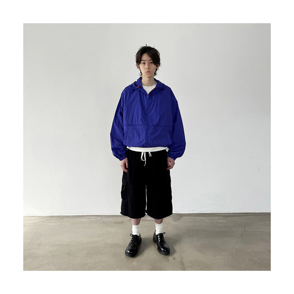 Person standing in black cargo shorts with a blue hooded jacket, white socks and black lace-up shoes