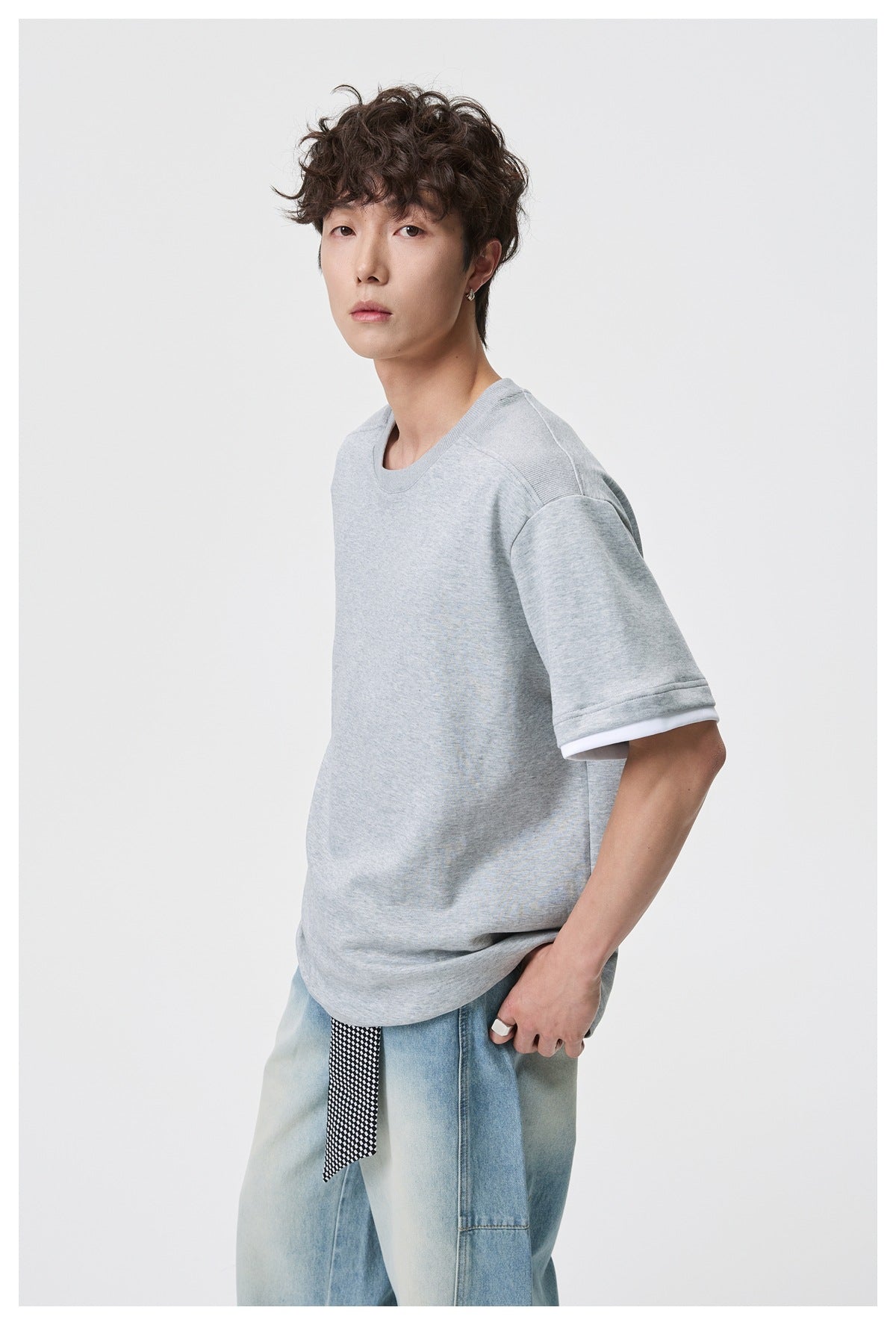 Angled view of a model wearing an oversized light gray tee with white sleeve trim.
