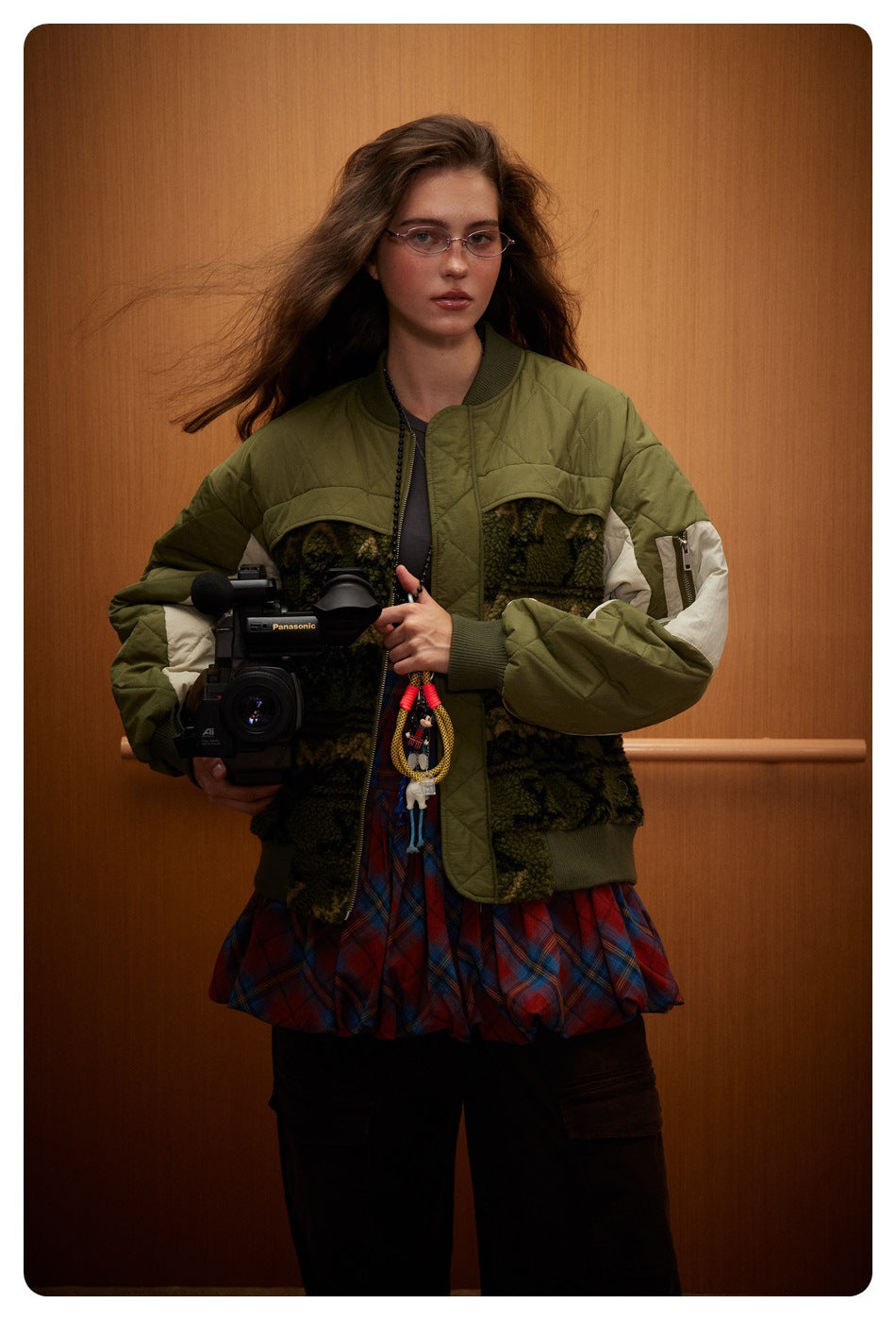Front view of a model wearing an olive quilted bomber jacket with dark patterned panels and cream sleeve accents.