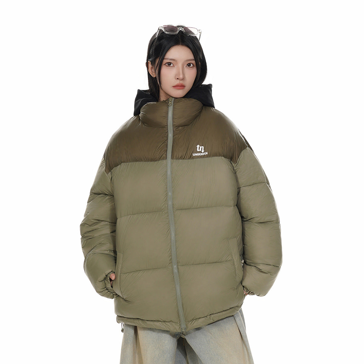 Front view of a model wearing a zipped olive puffer jacket with a dark brown upper panel and black hood.