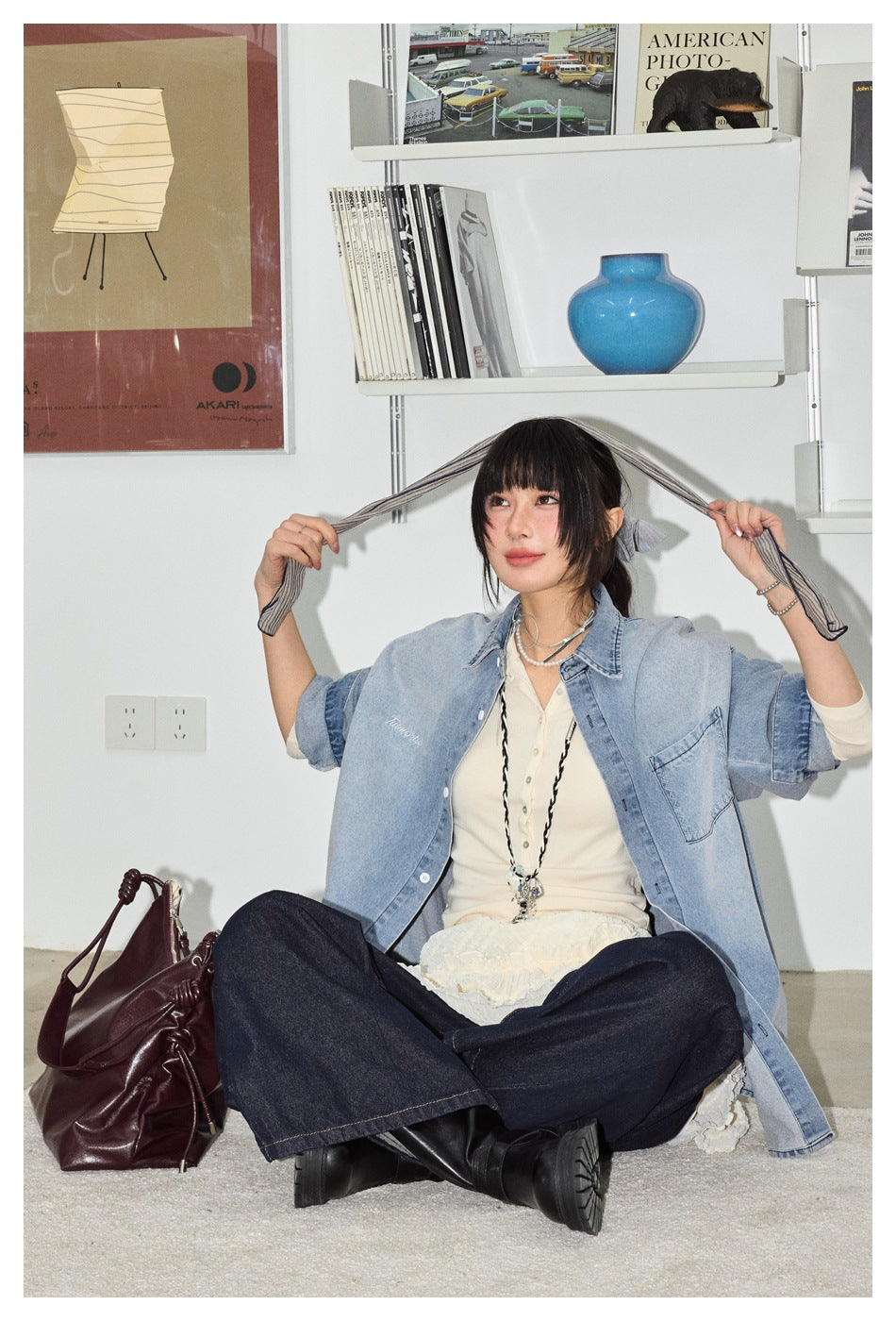 Seated model wearing an oversized light blue denim shirt with rolled sleeves and a chest pocket.