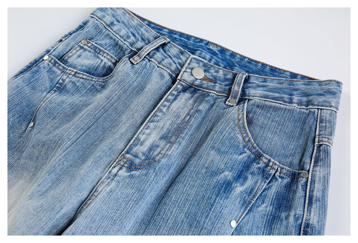 Angled close-up of the front waistband, button, belt loops, and curved pockets on faded blue jeans.