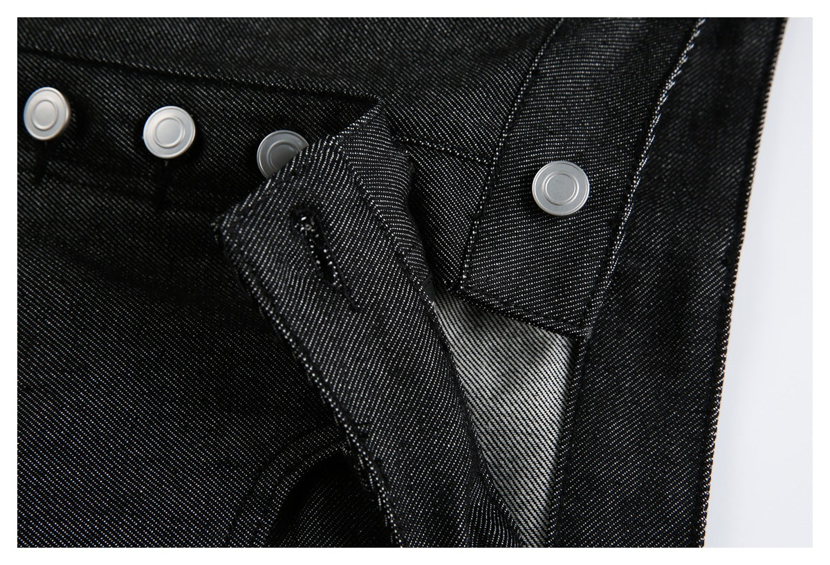 Close-up of black denim trousers showing silver metal waist buttons and the fly opening.