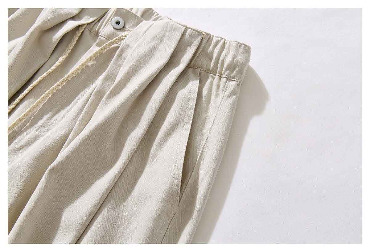 Angled close-up of cream trousers showing the gathered waistband, front button, pleats, and slanted pocket.