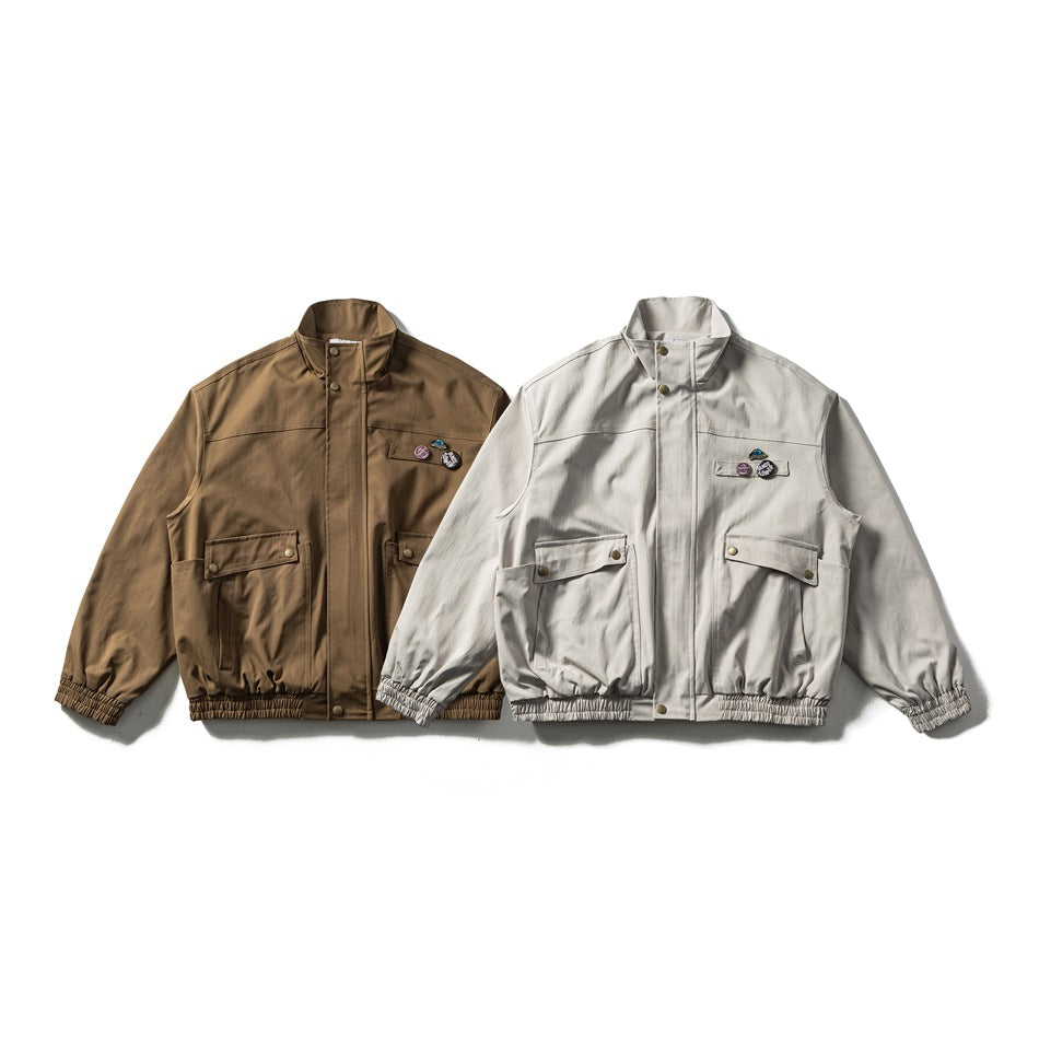 Front view of two jackets with stand collars, snap closures, flap pockets and gathered hems in brown and light beige.